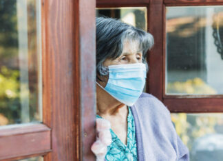 Mental health stable during pandemic, depression worse in seniors, study finds – Image of senior woman with a mask looking wistfully out a door
