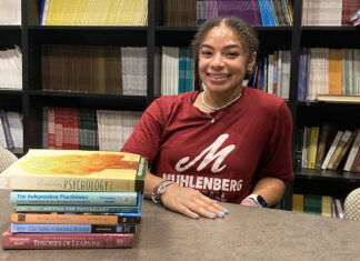 Latest News: Rising Senior Researches Athlete Mental Health A college student smiles while sitting next to a stack of psychology books
