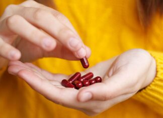 6 Vitamins and Minerals You Need to Age Gracefully, According to Experts A close-up of a person picking a red vitamin out of a handful of red vitamins in their other hand while wearing a bright yellow sweater.