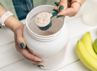 Collagen: Considering Its Health Benefits Beyond the Anti-Aging Claims A person with green nails and a smartwatch scooping a white collagen powder out of a container next to a banana and two green apples.