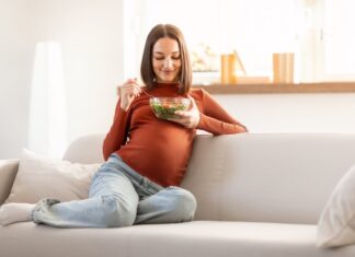 Better infant growth linked to healthy prenatal diet following USDA guidelines Pregnant woman enjoying a fresh vegetable salad while relaxing on a sofa indoors