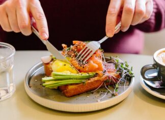 Do You Really Need Three Meals a Day? A Dietitian Sets the Record Straight A man's hands cutting a salmon and avocado flatbread with a knife and fork.