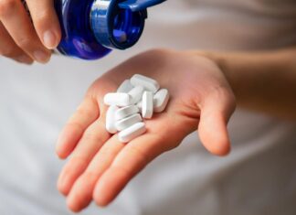 Can NAD+ Supplements Reverse the Aging Process? A person pouring white pills into their hand out of a blue pill bottle.