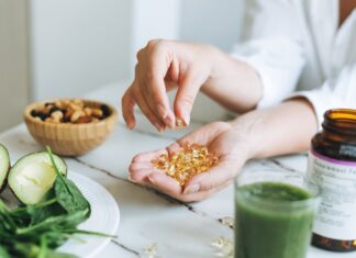 One gram of omega-3 per day may slow down the rate of biological aging Woman doctor nutritionist hands in white shirt with omega 3, vitamin D capsules with green vegan food.