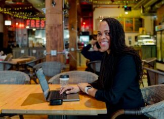 Uchechi Mitchell: Detecting if racial inequities make people age faster A woman smiles while sitting at a computer in a cafe.